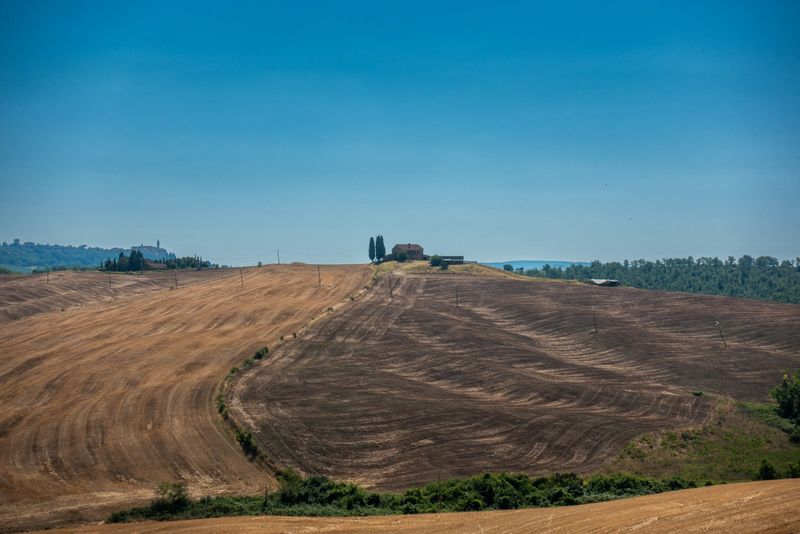 Campi agricoli mietuti su colline con un casale isolato in lontananza