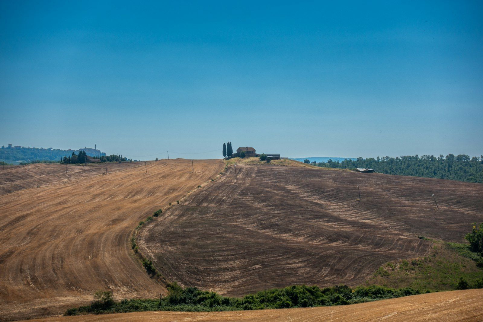 Campi agricoli mietuti su colline con un casale isolato in lontananza