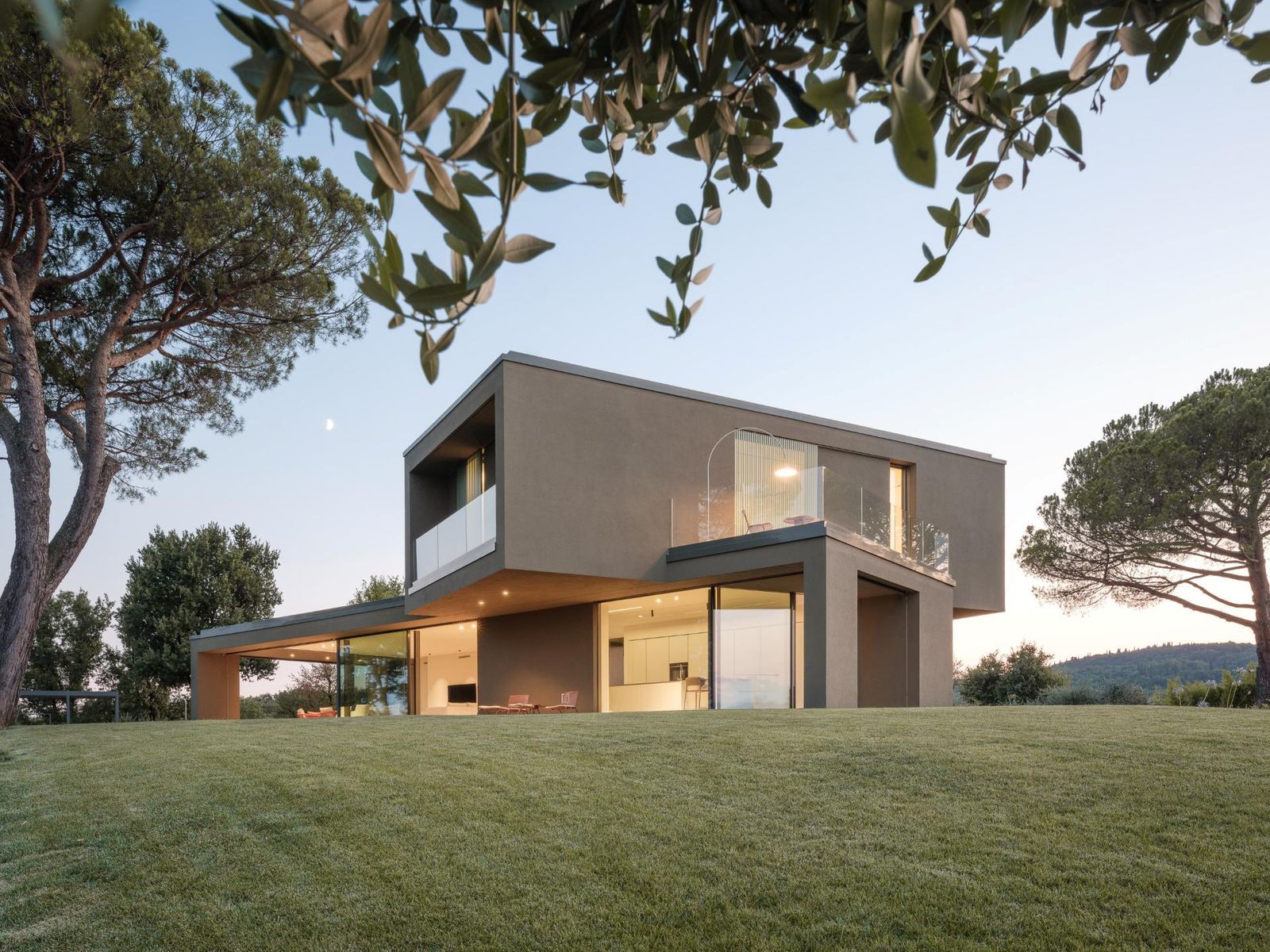 Villa contemporanea ILLE con volume superiore a sbalzo color terra, vetrate al piano terra e prato fra pini