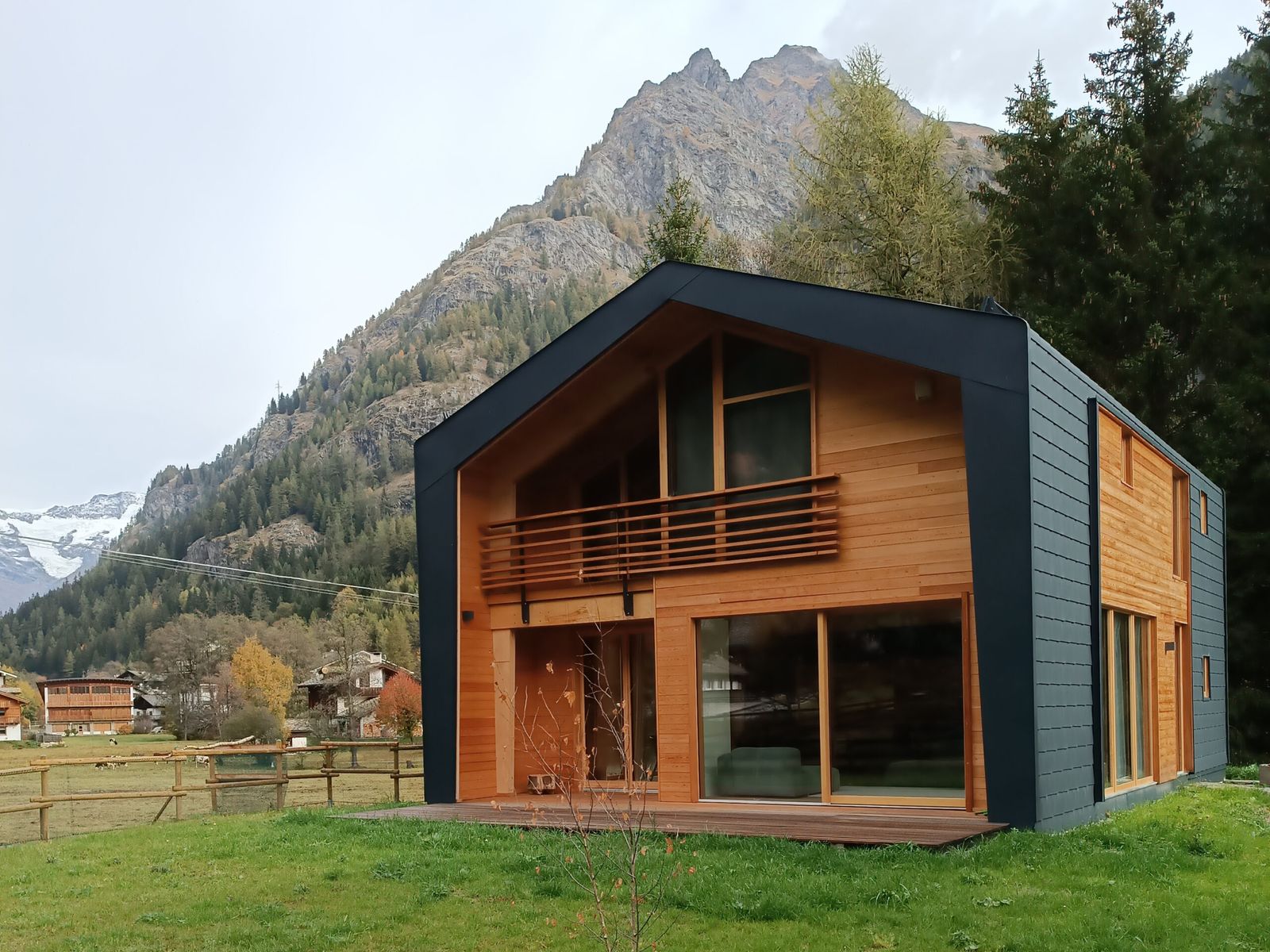Casa a due piani con cornice grigio scuro e facciata in doghe di legno, su un prato con la montagna e il ghiacciaio sullo sfondo