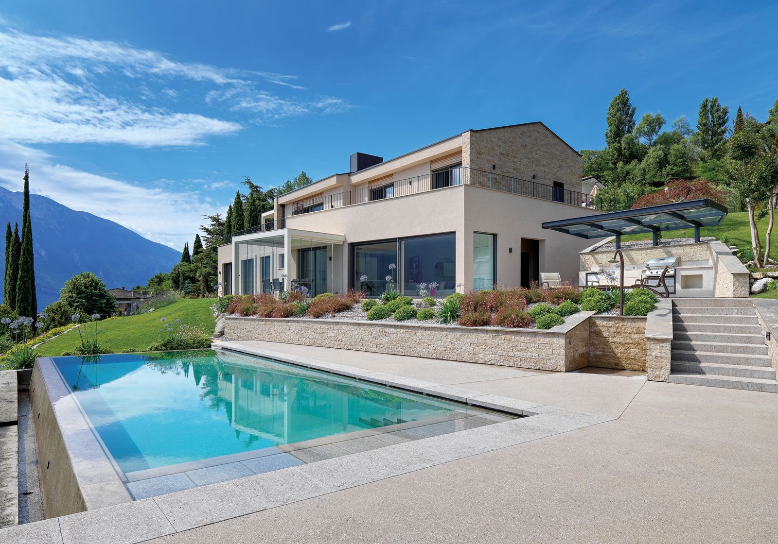 Villa a due piani con facciate in pietra e intonaco chiaro, piscina a sfioro in primo piano e montagne del Garda sullo sfondo