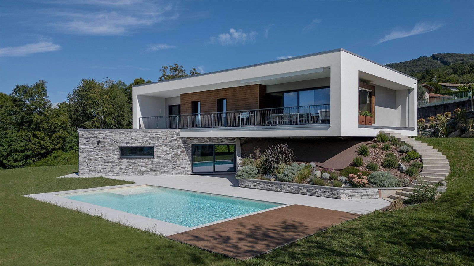 Villa moderna bianca con terrazza a sbalzo sopra un basamento in pietra, scala esterna curva e piscina sul prato in pendio