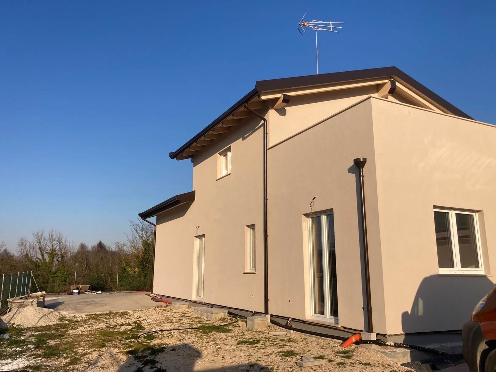 Casa in legno a due piani intonacata color sabbia, con tetto a falde e cortile in ghiaia sotto il cielo terso