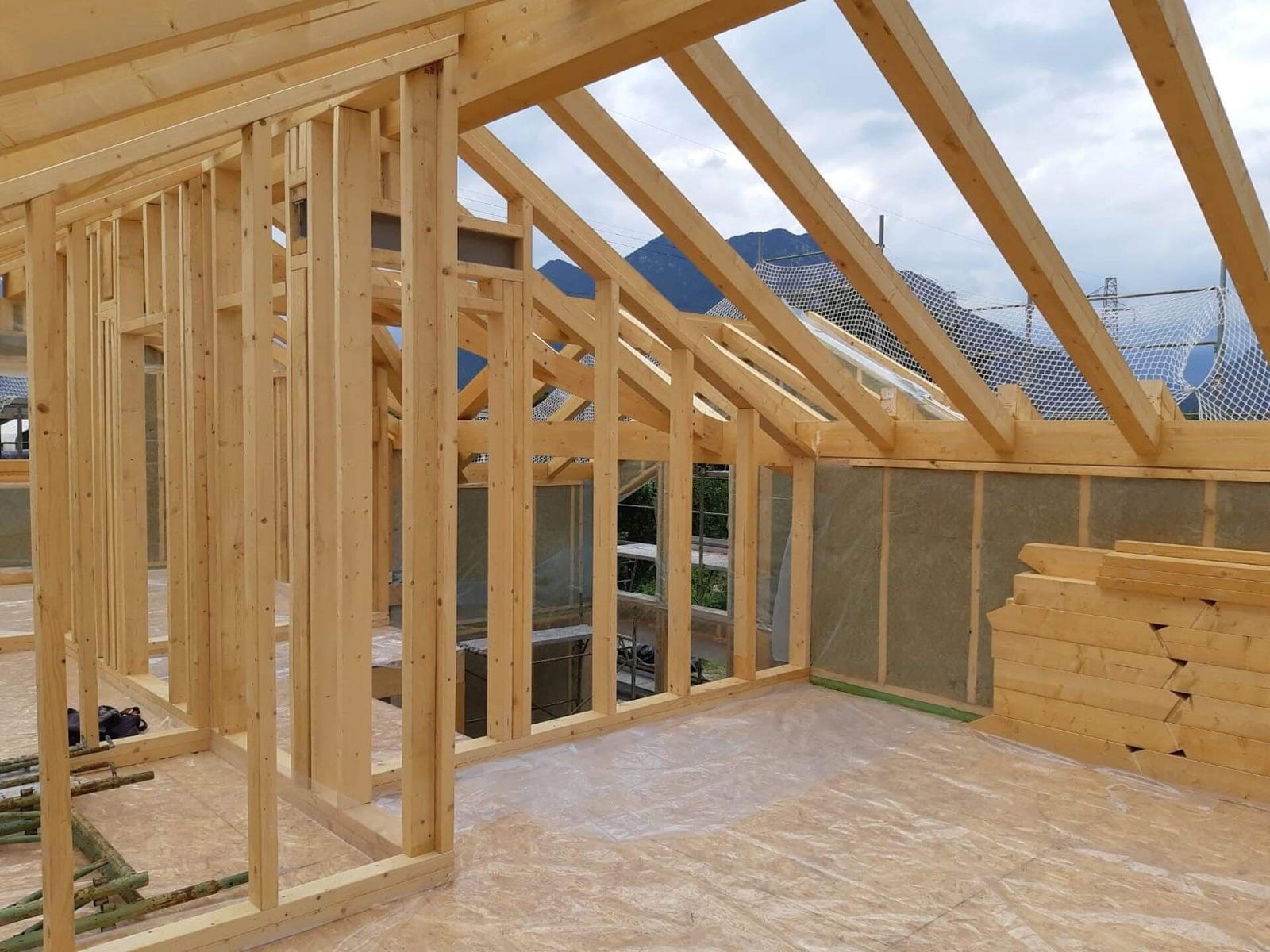 Struttura a telaio in legno con montanti, travi del tetto e pannelli isolanti, con le montagne sullo sfondo