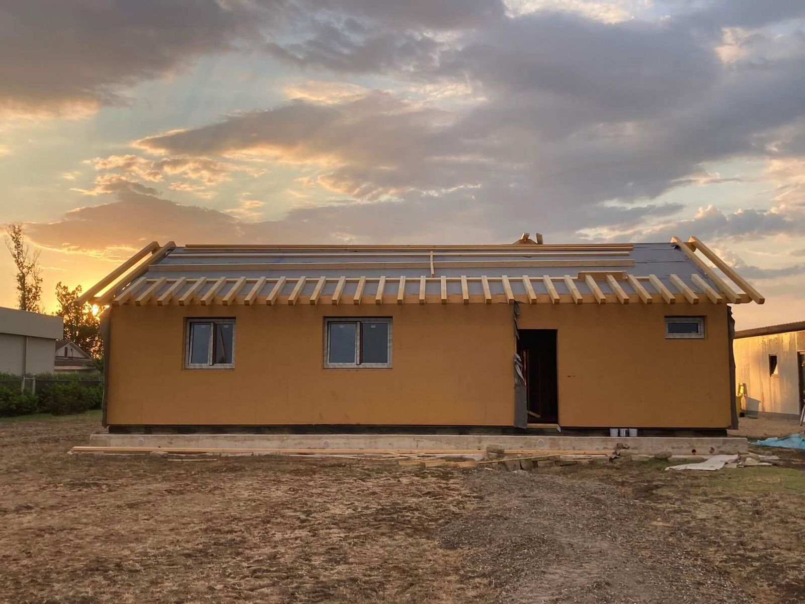 Casa in legno a un piano in costruzione, con pareti chiuse, finestre montate e travi del tetto a vista, al tramonto