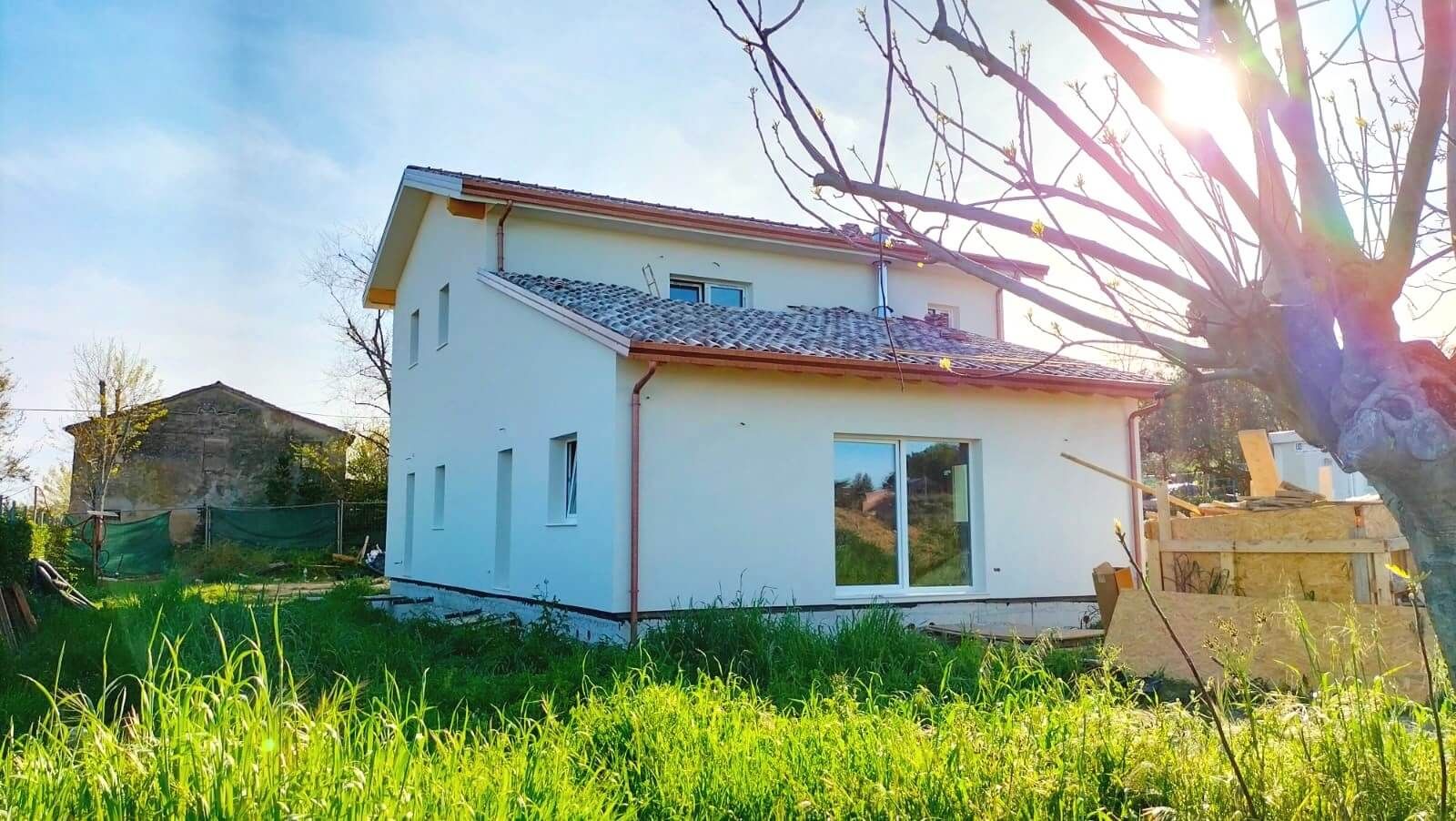 Casa in legno a due piani intonacata di bianco, con tetto in coppi e prato in controluce