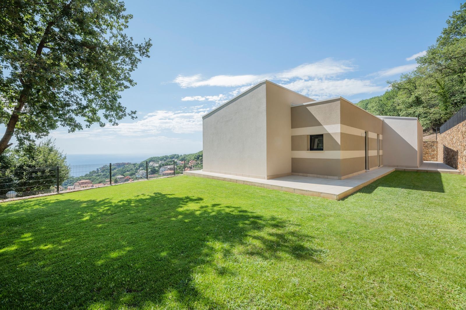 Casa in legno intonacata su un unico piano, con prato e vista sul mare della Riviera ligure