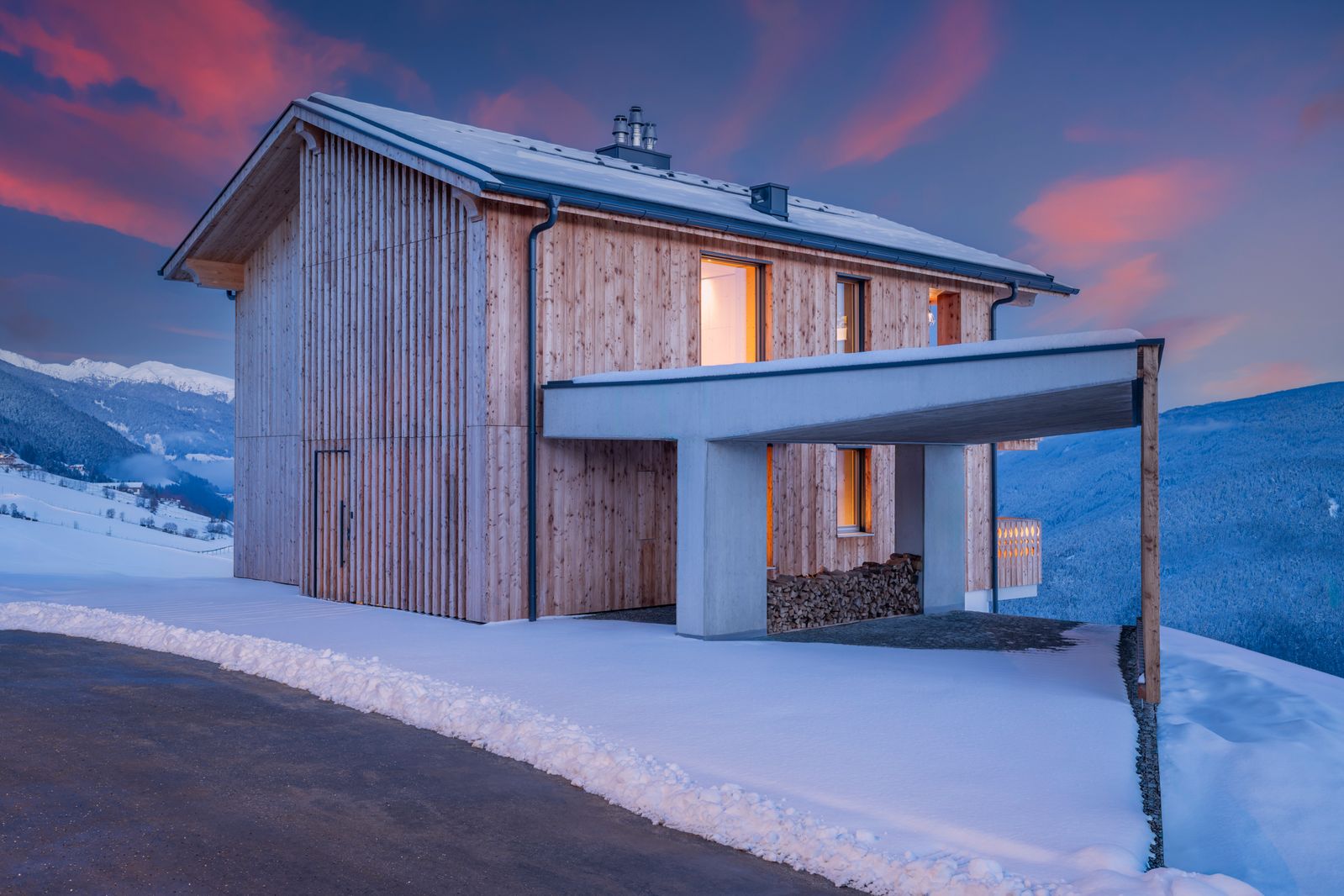 Casa in legno rivestita in larice con tettoia, nella neve con le montagne alle spalle