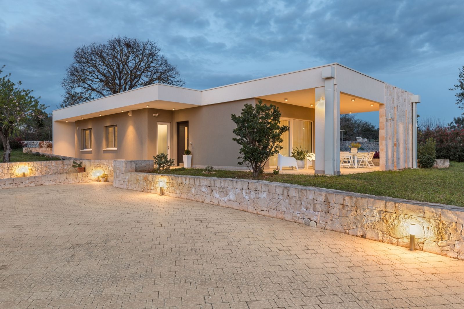 Casa in legno a un piano con portico e muretti a secco illuminati, in campagna al crepuscolo