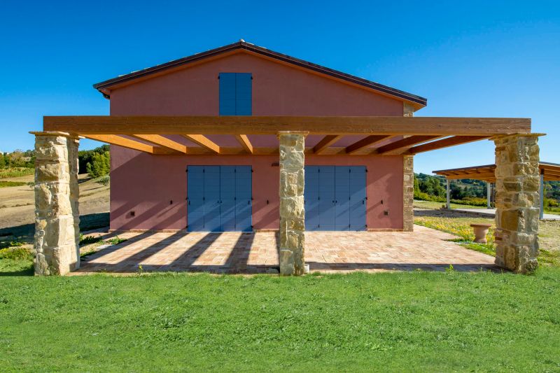 Casa in legno Subissati a Cupramontana, a due piani con facciata intonacata rosa, scuri azzurri e porticato in legno su pilastri in pietra
