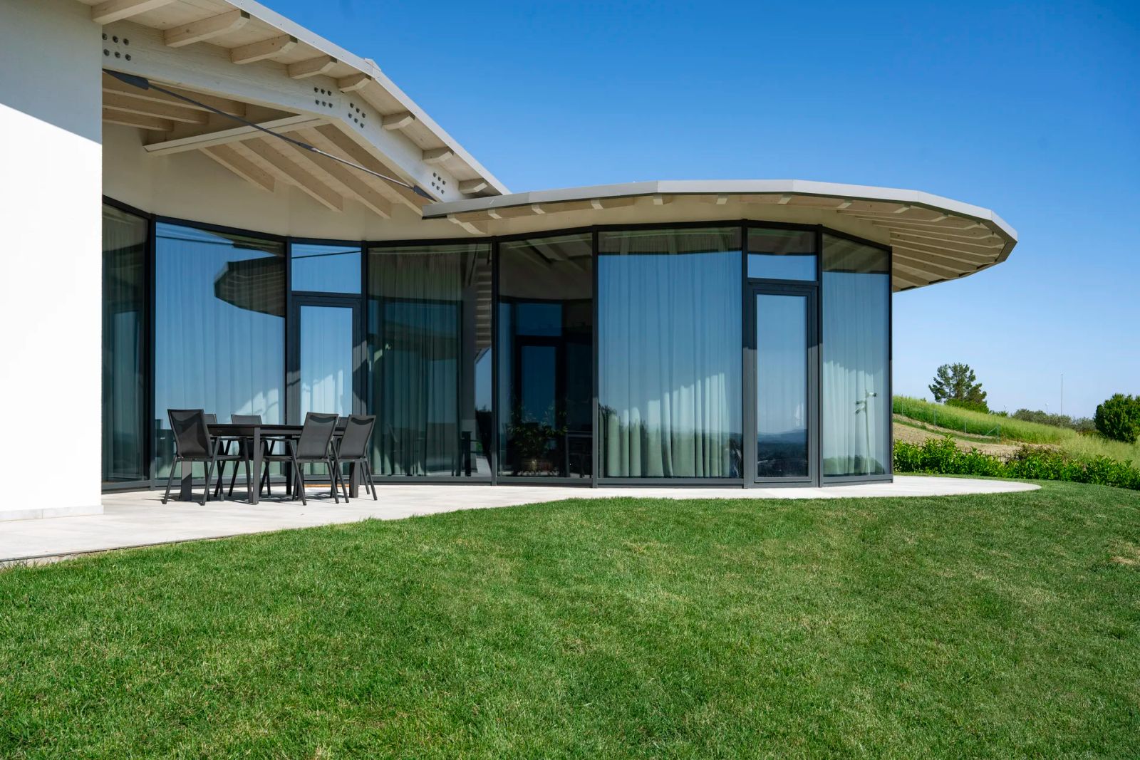 Villa contemporanea in legno Subissati con pareti vetrate curve sotto una copertura sporgente e terrazza sul prato