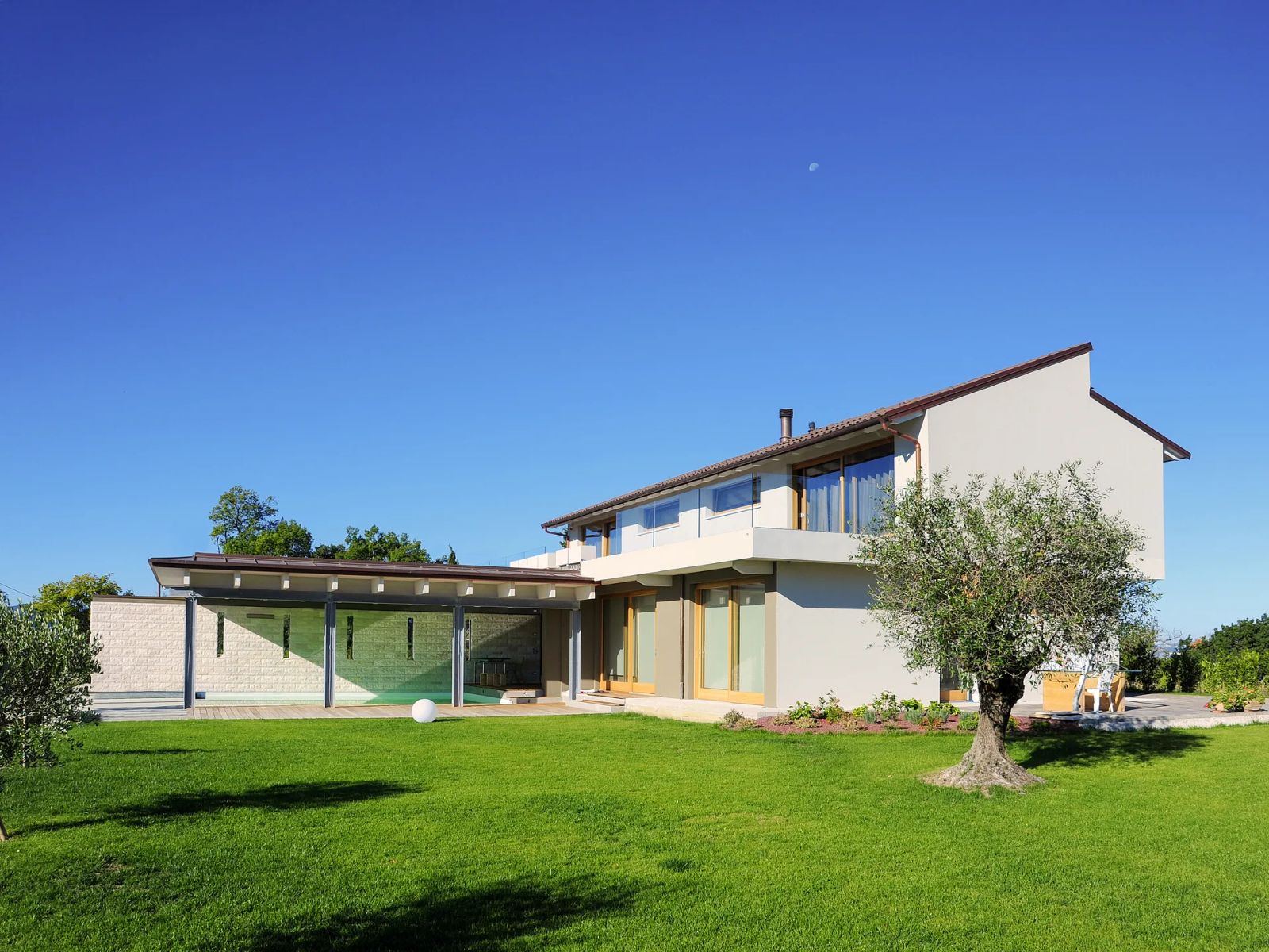 Villa in legno Subissati su due livelli con volume vetrato basso per la piscina coperta, olivo e prato in primo piano