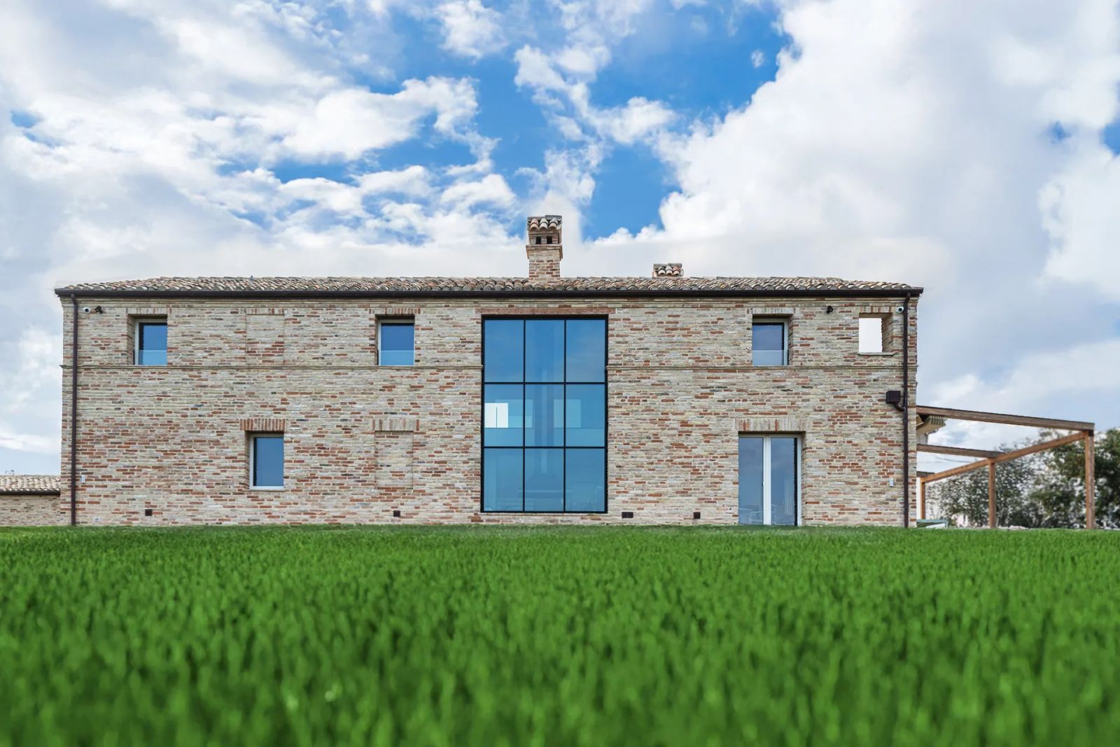 Villa Subissati con facciata in mattoni a vista, grande vetrata centrale a tutta altezza e prato in primo piano