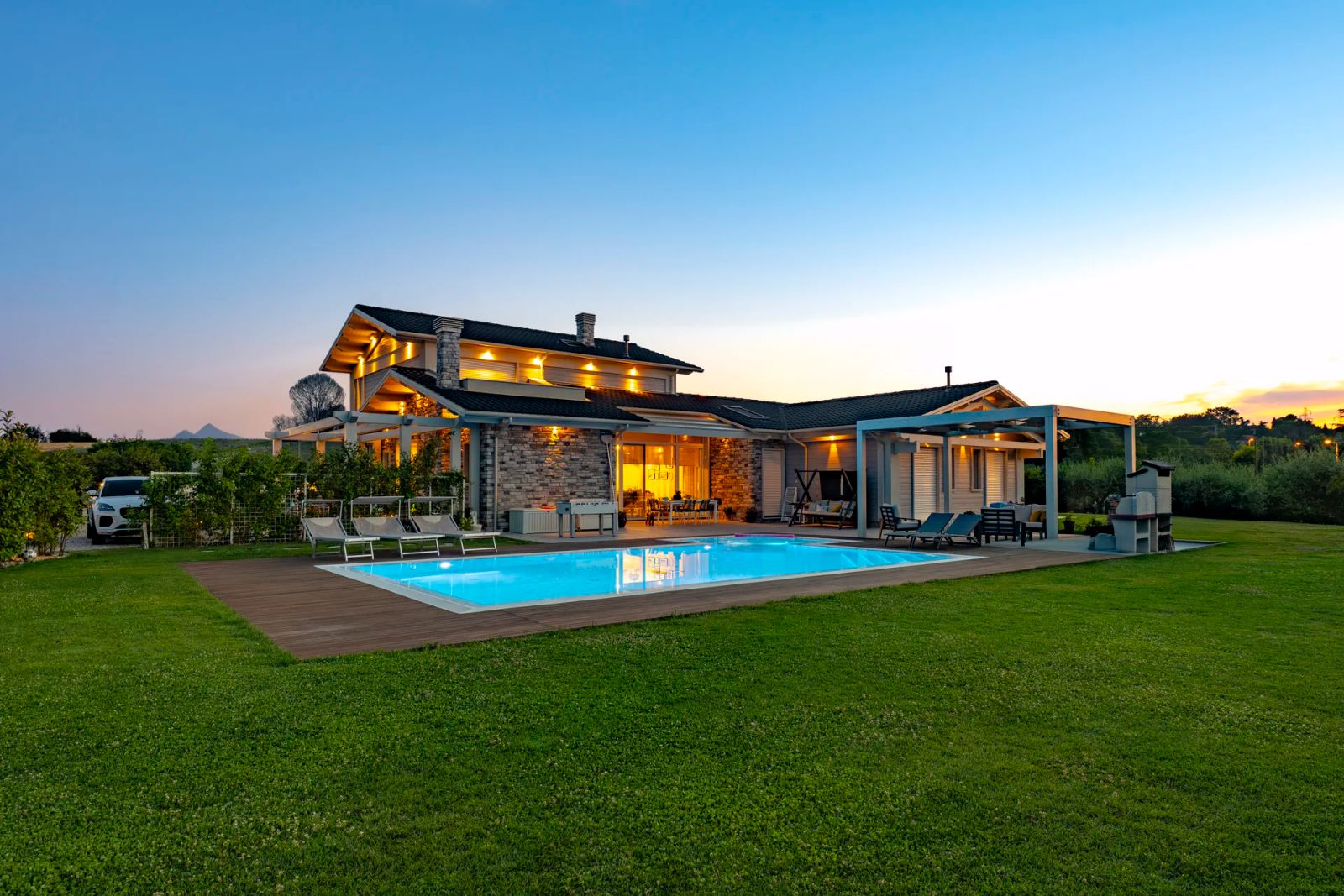 Villa unifamiliare in legno Subissati al tramonto, con luci accese, portico, pergolato e piscina sul prato nell'entroterra di Rimini