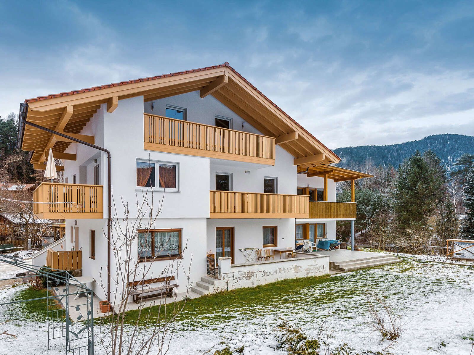 Casa in legno bianca su tre livelli con balconi in legno chiaro e tetto a capanna, nel giardino innevato di montagna