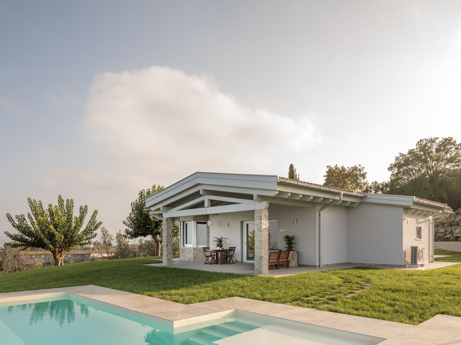 Casa Sabia di Wolf Haus su un piano, con portico su pilastri in pietra, prato e piscina in primo piano