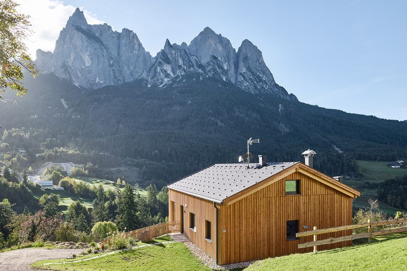 Chalet Arja di Wolf Haus rivestito in larice su un pendio erboso, con le montagne sullo sfondo