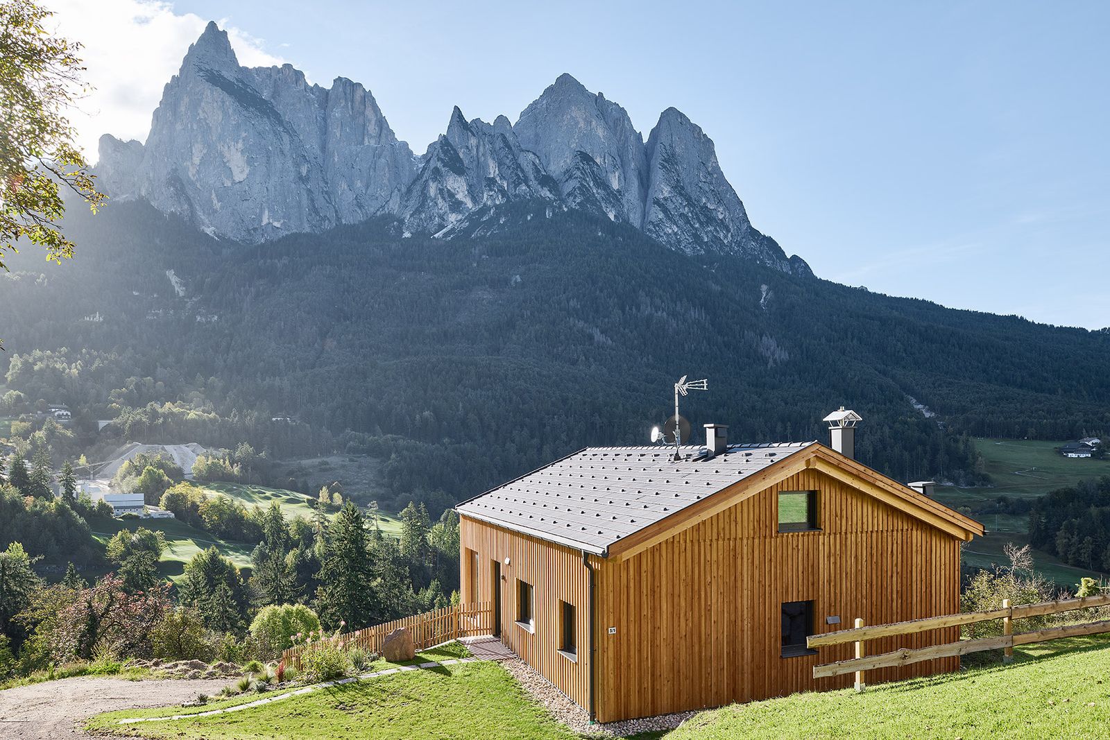 Chalet Arja di Wolf Haus rivestito in larice su un pendio erboso, con le montagne sullo sfondo